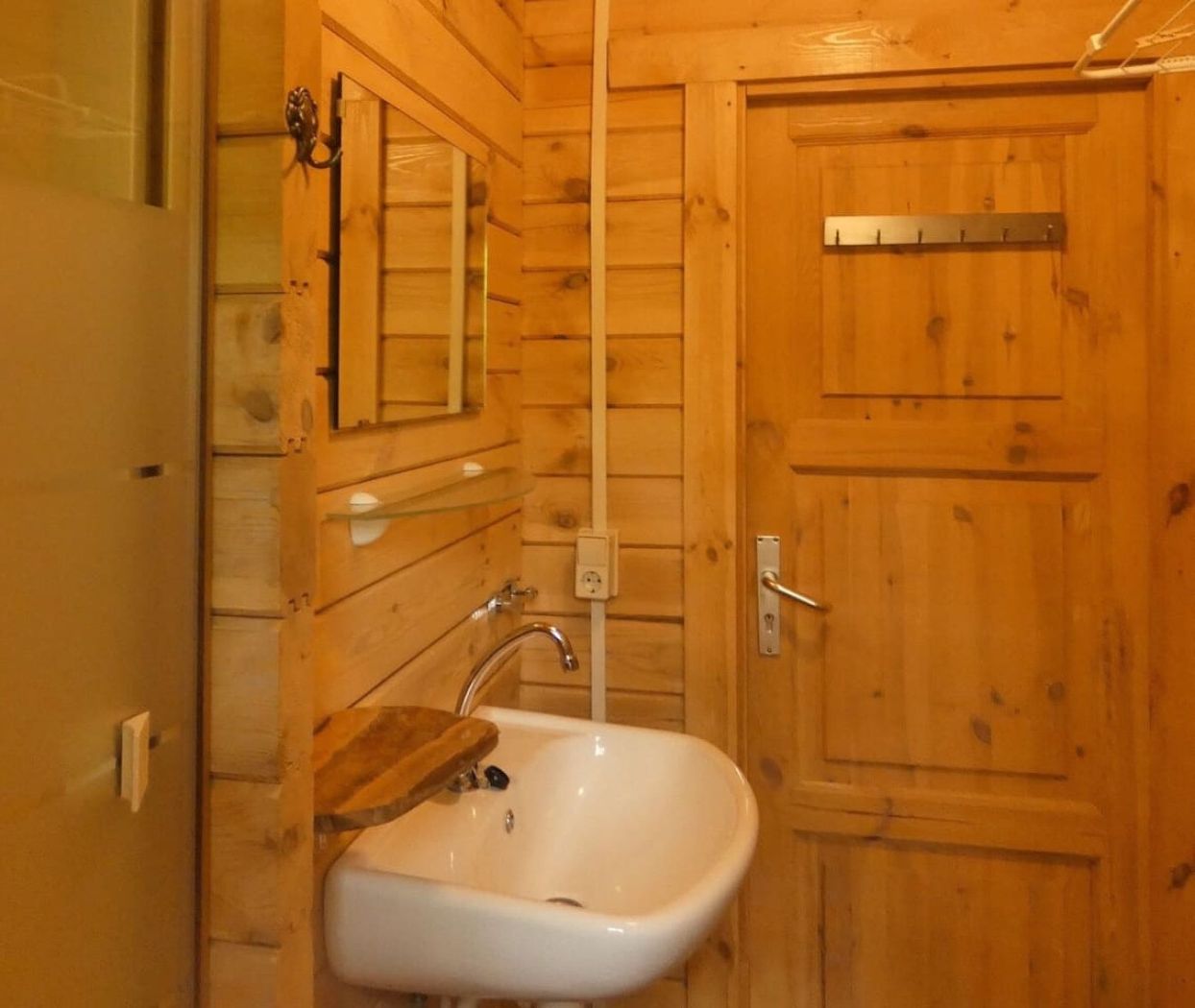 Une salle de bain en bois avec un lavabo blanc, des murs en bois et une porte ornée d’une plaque métallique.