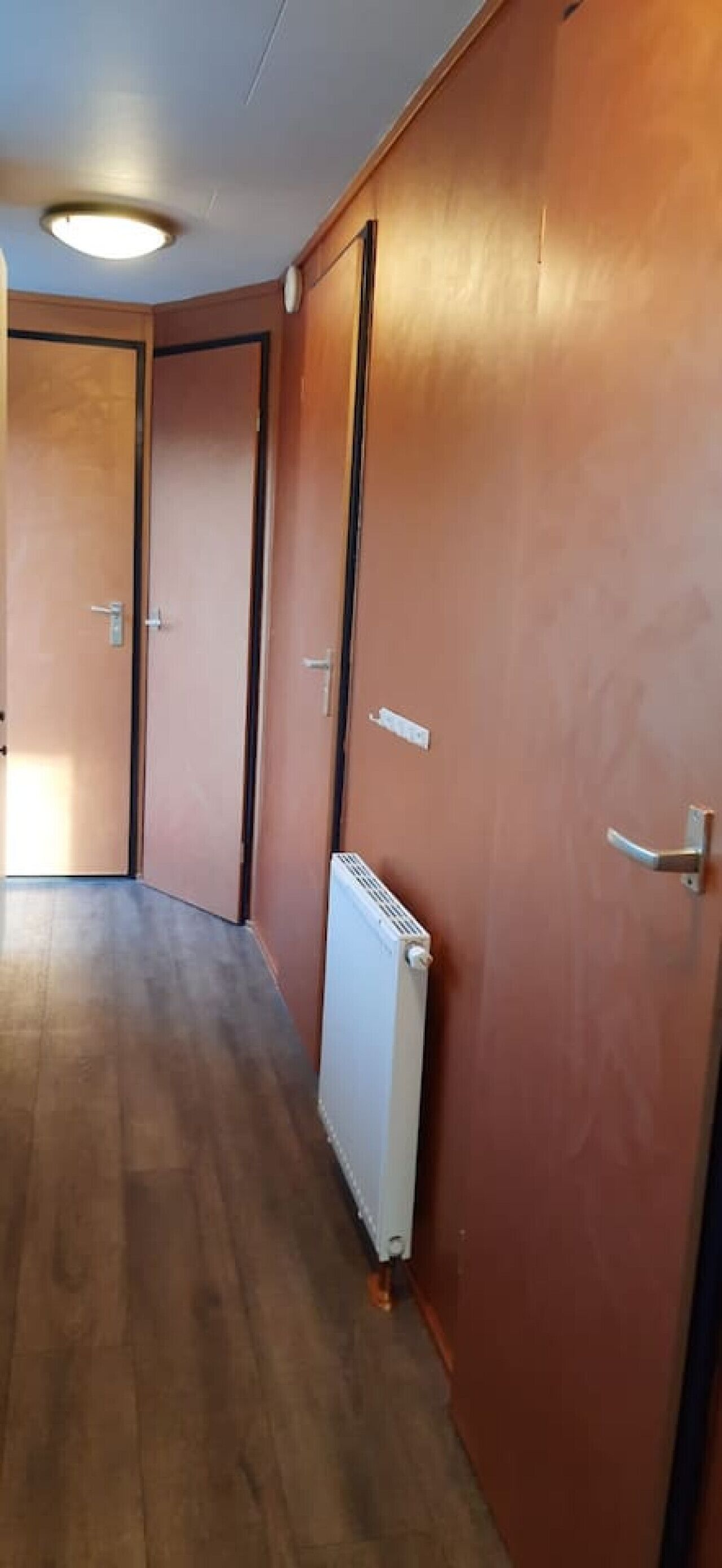 A hallway with wooden flooring, a radiator, and doors with handles.