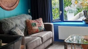 Een moderne woonkamer met een blauwe accentmuur, een groot raam met uitzicht op groen, een kamerkleed met patroon en een ronde oranje lamp.