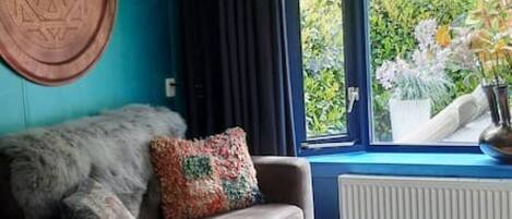 Una sala de estar moderna con una pared azul de acento, un ventanal con vistas a la vegetación, una alfombra estampada y una lámpara redonda naranja.