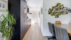 Ett modernt kök med mörka skåp, en matplats med grå stoppade stolar och en vägginstallation i form av konstverk.