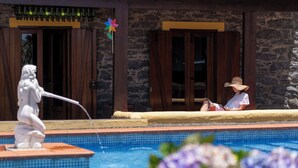 A pool area with a statue, a person relaxing by the pool, and a stone building in the background. - With pool and barbecue - Villa Roque (Ponta do Pargo)