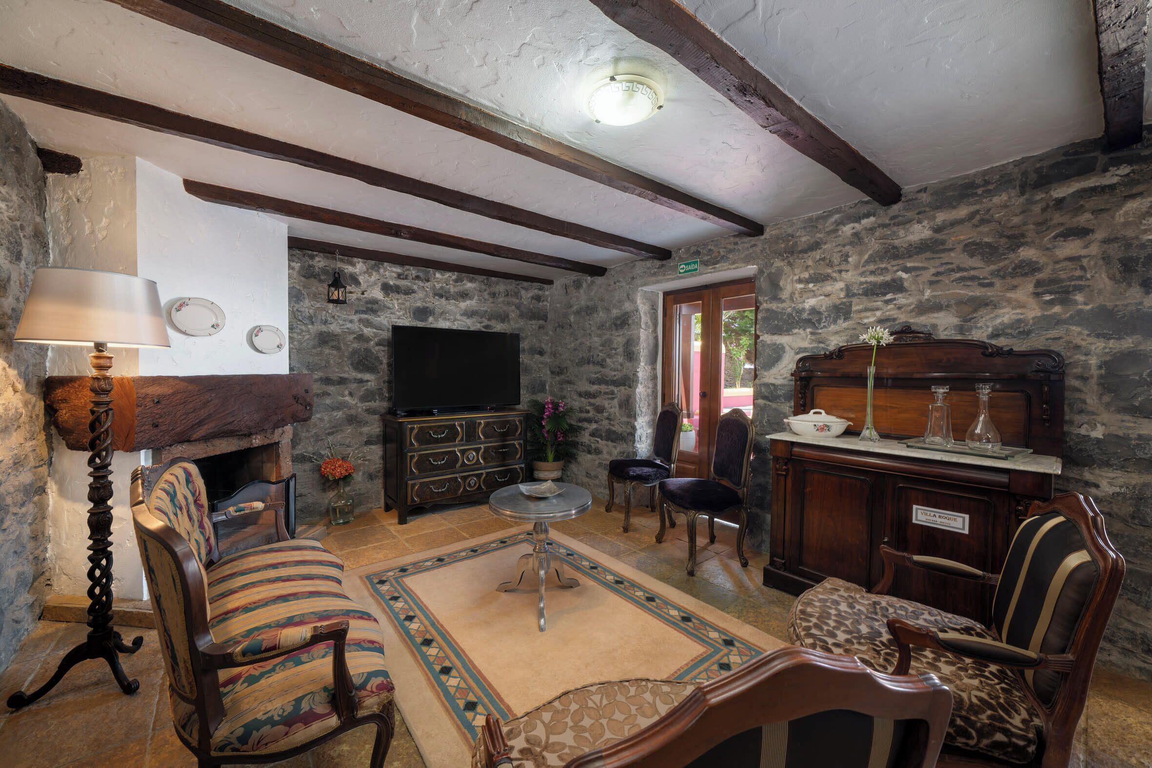 A rustic living room with exposed beams, a fireplace, a television, and vintage furniture.