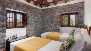 A room with two beds, stone walls, wooden beams, and windows with wooden shutters. - With pool and barbecue - Villa Roque (Ponta do Pargo)
