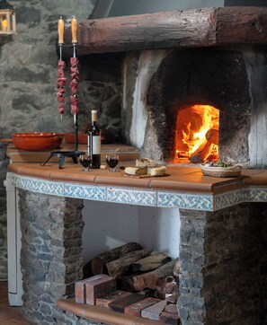 Une cheminée en pierre avec un poêle à bois, une bouteille de vin et un bol posés sur le manteau.