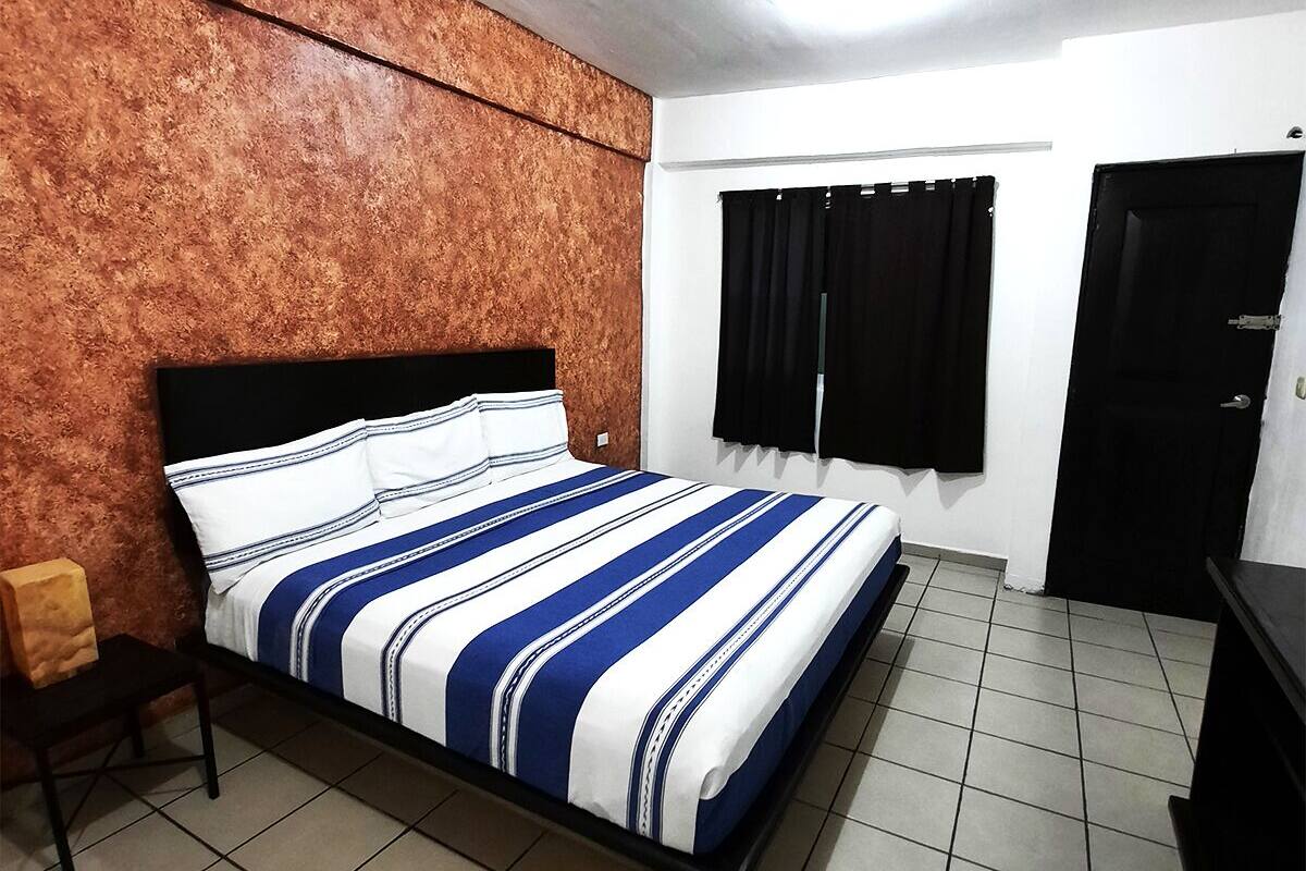 A bedroom with a bed, a nightstand, a window with curtains, and a door.