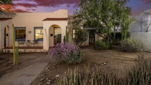 A stucco building with arched doorways, a patio with chairs, and a cactus in the foreground. - Charming / Outdoor Dining / 1 BR 1 BA / Sam Hughes (Tucson)