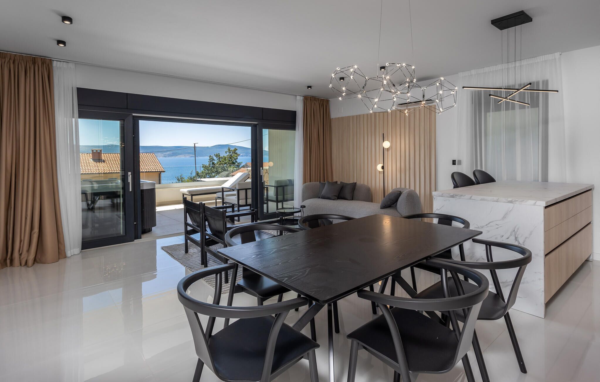 Una sala moderna con comedor, un sofá, una isla de cocina de mármol y vista al mar.