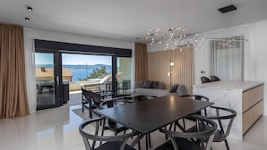 Ein modernes Wohnzimmer mit Essbereich, einer Couch, einer Marmorküche mit Kochinsel und Blick aufs Meer.