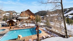 Eine Holzlodge mit Schwimmbad, umgeben von schneebedeckten Hügeln und Bäumen.