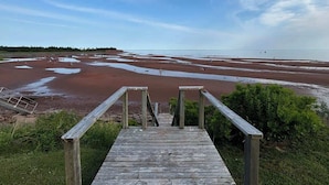 A wooden staircase leading to a beach with red sand and a clear sky.