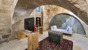 A cozy room with a stone arch, a wooden coffee table, a sofa, and a television. - Obruk Kervansaray Museum Hotel (Konya)
