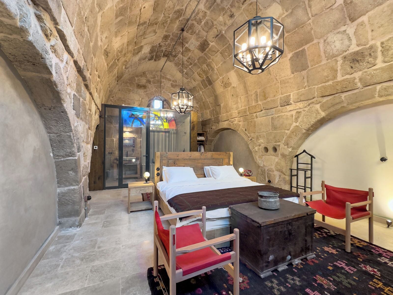 A stone-walled bedroom with a wooden bed, a red chair, and a small table.
