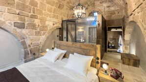 A stone-walled bedroom with a wooden bed, a mirror, and a vintage telephone. - Obruk Kervansaray Museum Hotel (Konya)