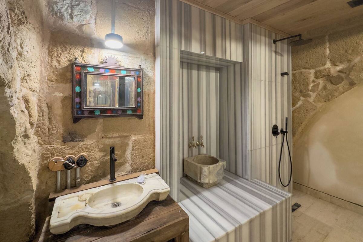 Un baño rústico con pared de piedra, lavabo de madera, espejo con adornos coloridos y zona de ducha.