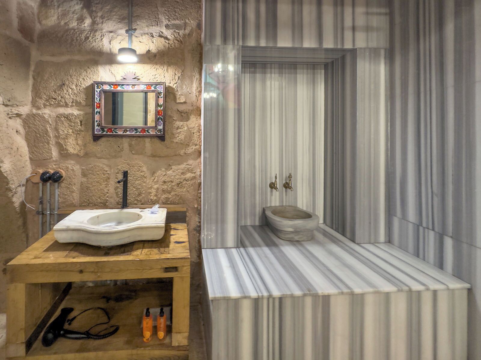 A rustic bathroom with a wooden vanity, a simple toilet, and a striped marble floor.
