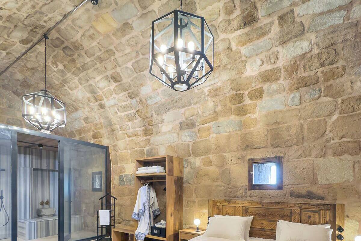 Un dormitorio rústico con techo de piedra, una cama grande, una mesita de noche de madera, una silla roja y una pequeña mesa con un cubo.