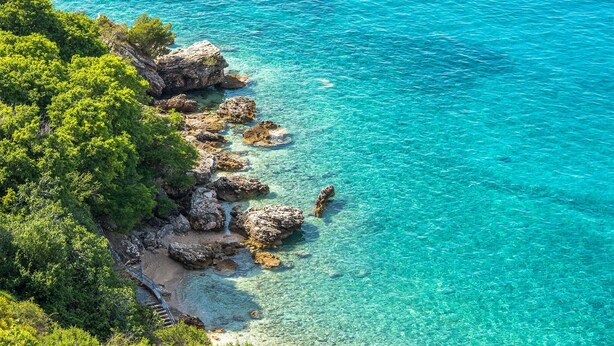 Paisagem costeira com águas turquesa cristalinas, formações rochosas e vegetação verde exuberante.