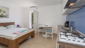 Quarto compacto com cama, mesa de cabeceira e uma pequena cozinha equipada com fogão a gás.