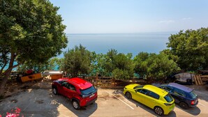 Uma área de estacionamento com três carros, um banco de madeira e vista para o mar.