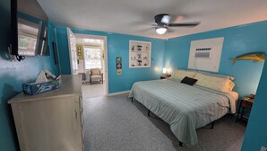 A bedroom with a bed, a desk, a chair, a ceiling fan, and a window.
