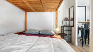 A bedroom with a wooden ceiling, a bed with white bedding, two pillows, a nightstand with a lamp, and a desk with a chair. - 1 bedroom nice apartment in Carnac (Carnac)