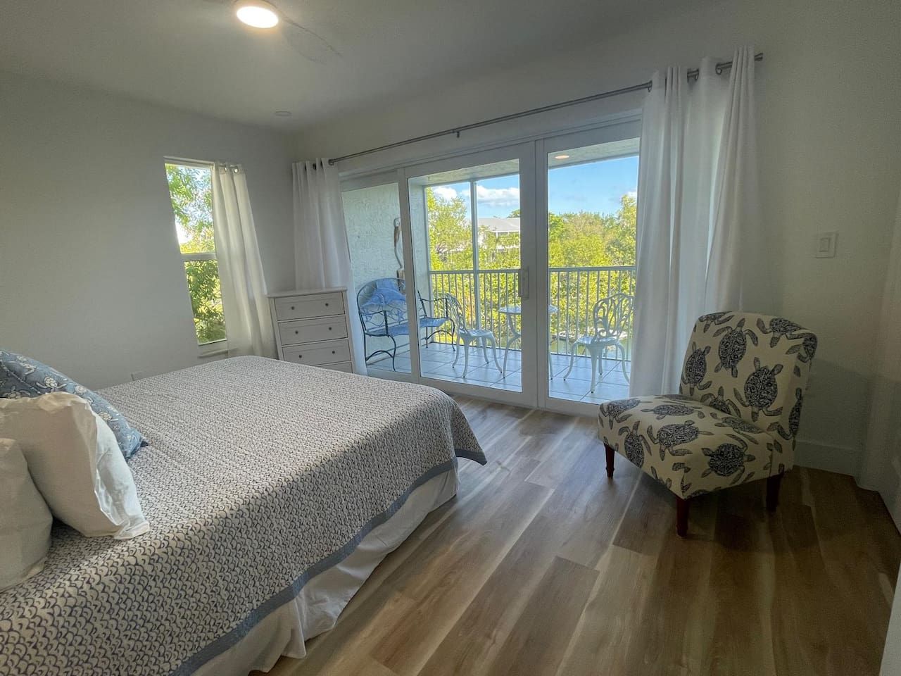 A bedroom with a bed, a chair, a balcony with a view, and a window.