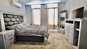 A bedroom with a bed, a TV, a dresser, and an air conditioning unit.
