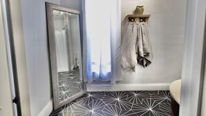 A bathroom with a geometric patterned floor, a mirror with a textured frame, a shower curtain, and a towel rack with towels.