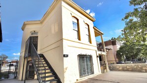 A two-story building with a beige facade, a metal staircase, and a gated entrance.