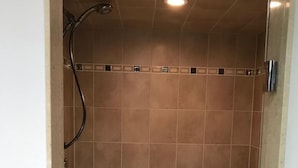 Une douche avec des murs carrelés et un pommeau de douche mobile.