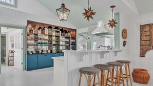Una cocina con una isla central, taburetes de bar y diverso menaje de cocina en estantes.