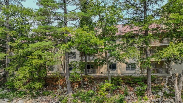 A multi-story building with balconies, surrounded by trees and a rocky stream. - Riverfront Oasis at Loon (Lincoln)