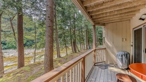 A wooden deck with a view of a forest and a river. - Riverfront Oasis at Loon (Lincoln)