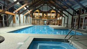Una piscina interior con suelo de baldosas y una zona de piscina más pequeña separada.