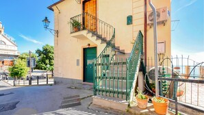 Un edifici amb una porta verda, una escala amb barana metàl·lica i plantes en testos al balcó.