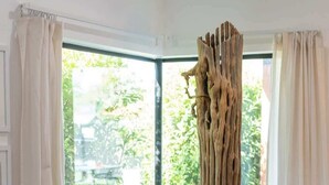 A room with a large window, a wooden tree trunk sculpture, a bench, and a view of greenery outside. - Complex | Theater, Pickleball & Pool in DT Phoenix (Phoenix)