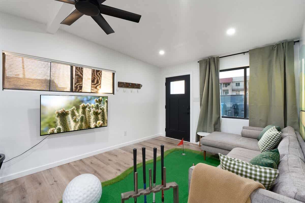 A living room with a flat-screen TV, a ceiling fan, a sofa with cushions, and a small table.
