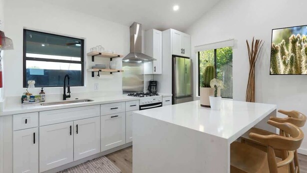 A modern kitchen with white cabinetry, a central island, and a large window providing a view of greenery. - Complex | Theater, Pickleball & Pool in DT Phoenix (Phoenix)