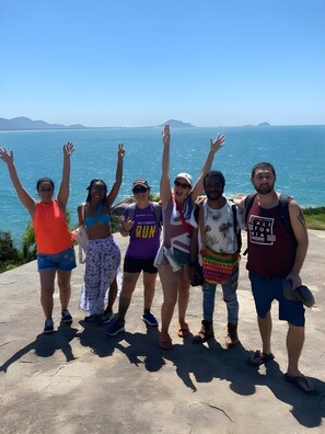 A group of people standing on a concrete ledge with a scenic ocean view in the background. - Nomades Riverside - Adventure Hostels & Coworking (Florianópolis)
