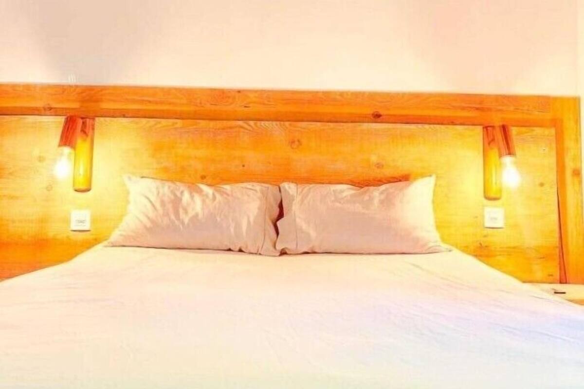 Une chambre à coucher avec une tête de lit en bois, deux lampes de chevet et un lit recouvert de linge de lit blanc.