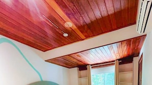 Una camera da letto con un letto, un tavolino, una finestra con tende e un soffitto in legno.