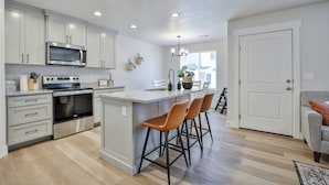 A modern kitchen with white cabinetry, stainless steel appliances, and a central island with bar stools.