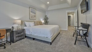 A bedroom with a bed, bedside table, chair, desk, lamp, and a TV mounted on the wall.