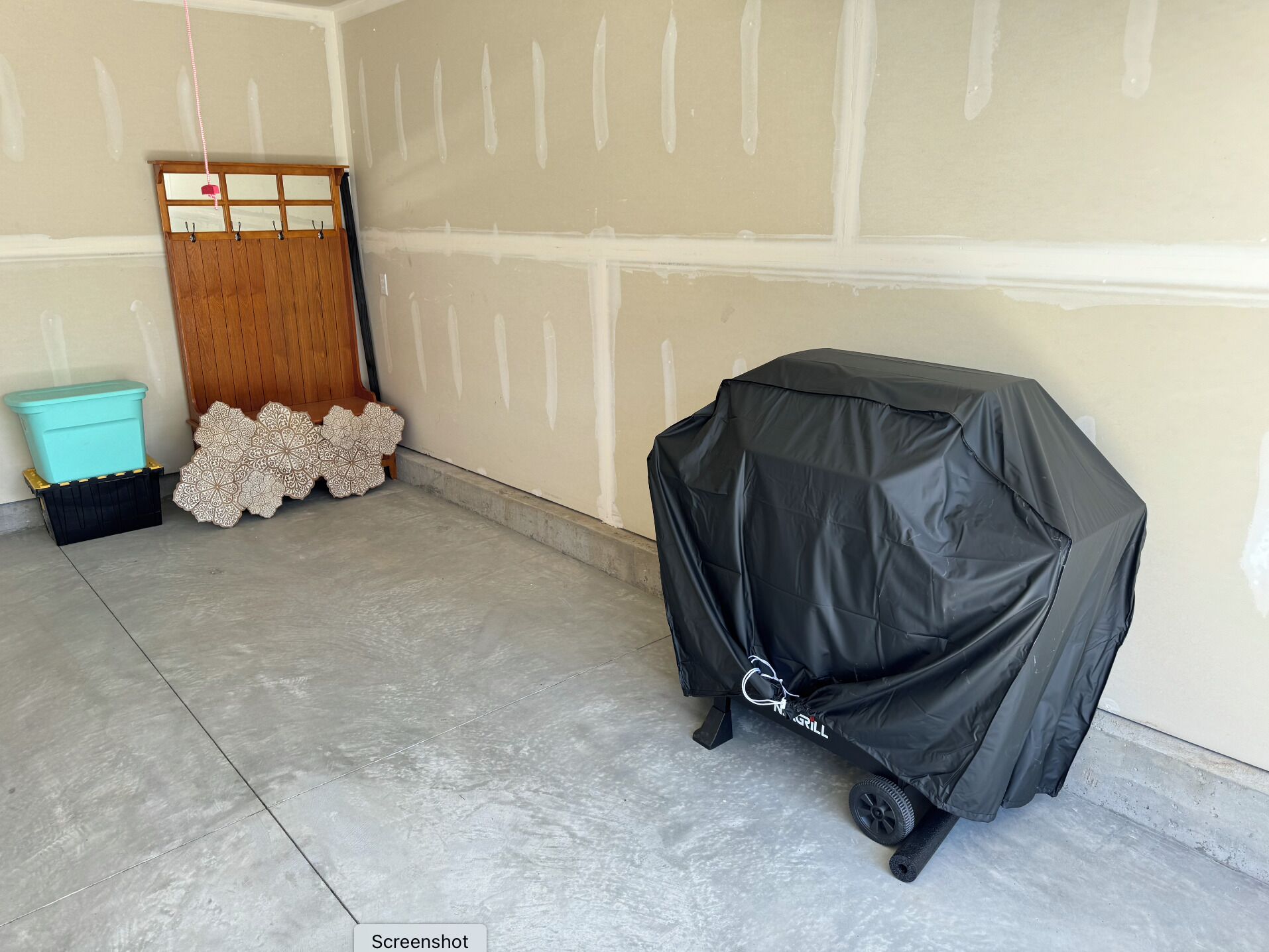 A garage with a covered grill, a wooden door, and a blue trash bin.