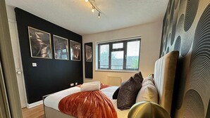 Une chambre à coucher avec un lit, une table de chevet, une lampe et une fenêtre avec des stores.