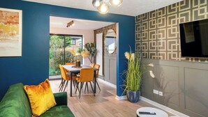 Un salon moderne avec un mur bleu, un canapé vert, un coin repas avec des chaises orange et une cuisine avec un revêtement mural à motifs.