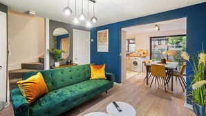 Un salon moderne avec un canapé vert, un coin repas et une cuisine visible à travers une porte ouverte.