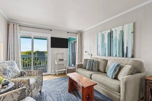 A living room with a sofa, a coffee table, a TV, and a balcony with a chair.