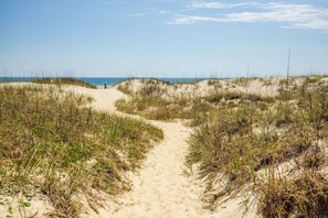A sandy path leading to a beach with dunes and sparse vegetation.